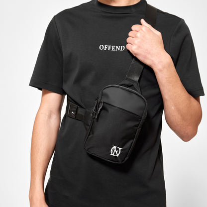 Close up of model wearing black 'OFFEND' T-Shirt with black 'OFFEND' crossbody bag with white 'OFFEND' logo in the bottom right of bag