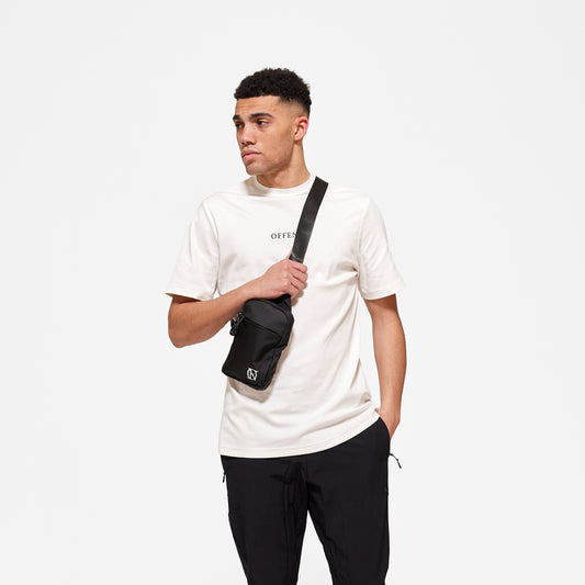 Model wearing white 'OFFEND' T-shirt with black 'OFFEND' text across centre of chest, wearing black crossbody bag with white 'OFFEND' logo in the bottom right hand corner of bag
