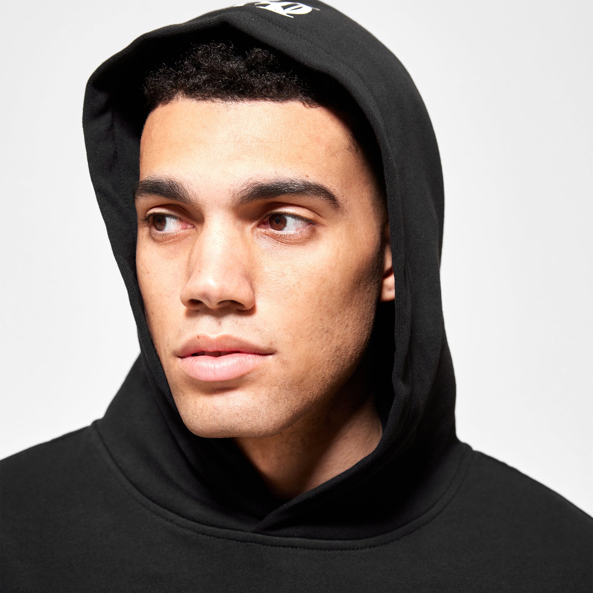 Close up of models face wearing the black 'OFFEND' hoodie with hood up, you can see the 'OFFEND' logo on top of the hood