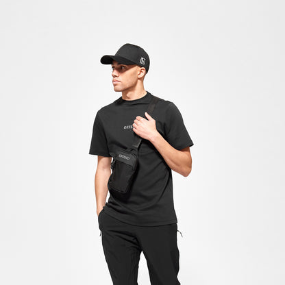 Model wearing 'OFFEND' black T shot from the front with 'OFFEND' text on chest wearing the classic 'OFFEND' cross body bag, wearing 'OFFEND' baseball cap
